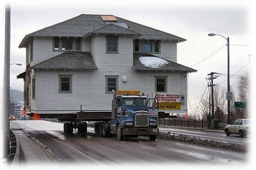 Casa de madeira sendo transportada por caminhão.